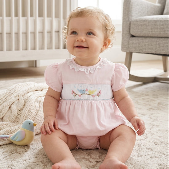 Baby girl wearing a Carriage Boutique pink bubble romper with hand-smocked bird embroidery and lace collar detail.