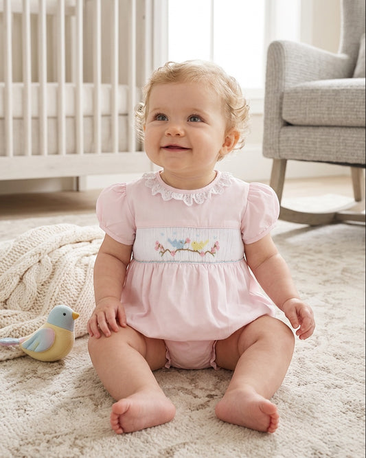 Baby girl wearing a Carriage Boutique pink bubble romper with hand-smocked bird embroidery and lace collar detail.