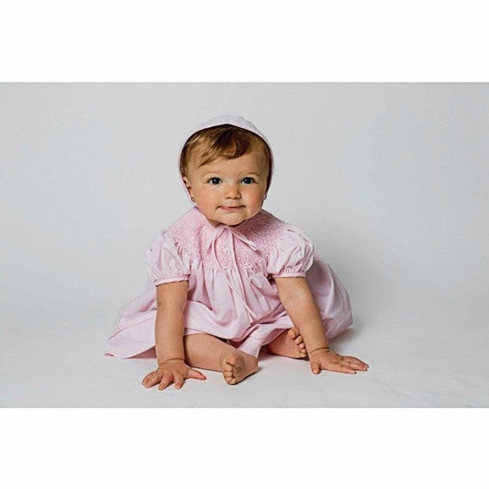 Carriage Boutique pink hand-smocked bishop dress with pearl cross detail and matching bonnet on baby girl.