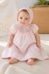 Carriage Boutique pink hand-smocked bishop dress with pearl cross detail and matching bonnet on baby girl.