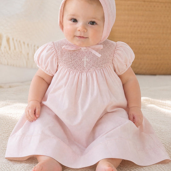 Carriage Boutique baby girl pink cotton bishop dress with hand-smocked pearl cross detail and matching bonnet