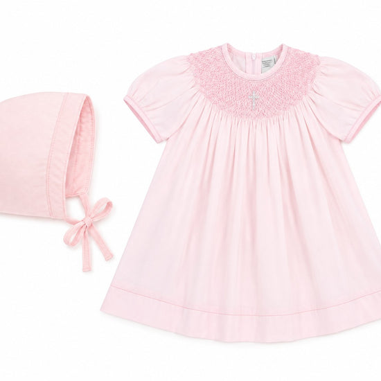 Carriage Boutique baby girl pink cotton bishop dress with hand-smocked pearl cross detail and matching bonnet.