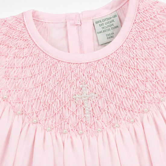 Carriage Boutique pink cotton baby christening bishop dress with hand-smocked detail and pearl cross embellishment.