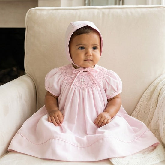 Carriage Boutique baby girl pink cotton bishop dress with hand-smocked pearl cross detail and matching bonnet