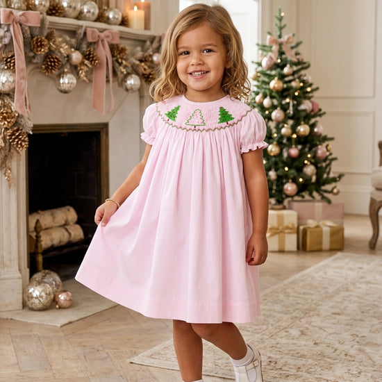 Toddler girl wearing a Carriage Boutique pink cotton bishop dress with hand-smocked Christmas tree embroidery.