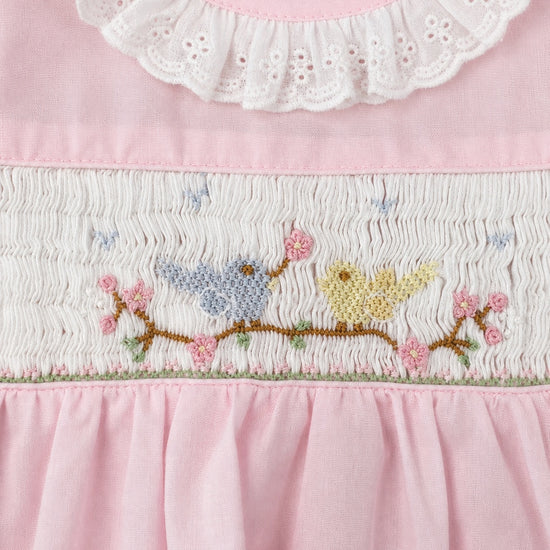 Carriage Boutique baby girl dress with pink fabric, white eyelet collar, and hand-smocked bird and flower embroidery.