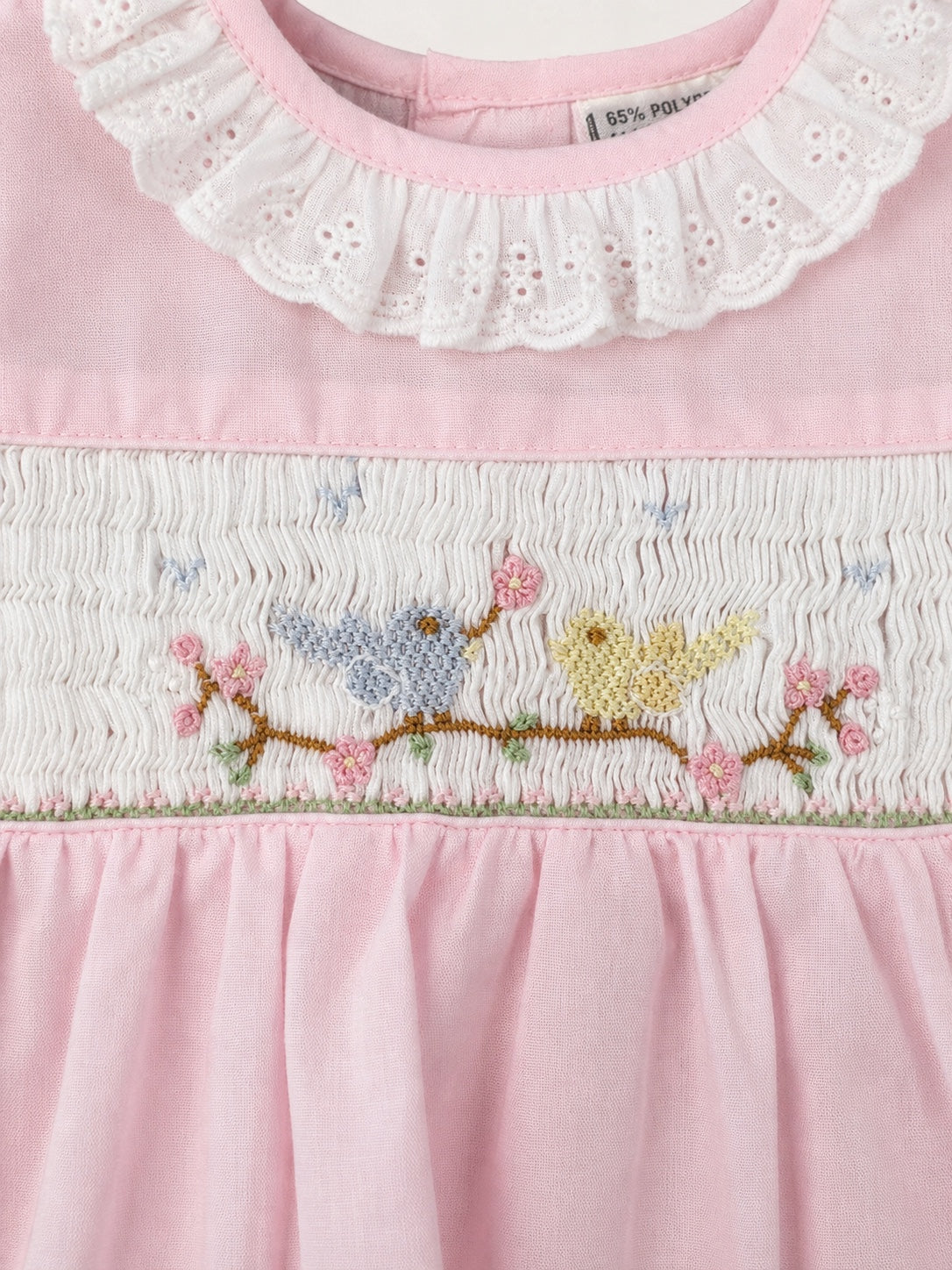 Carriage Boutique baby girl dress with pink fabric, white eyelet collar, and hand-smocked bird and flower embroidery.