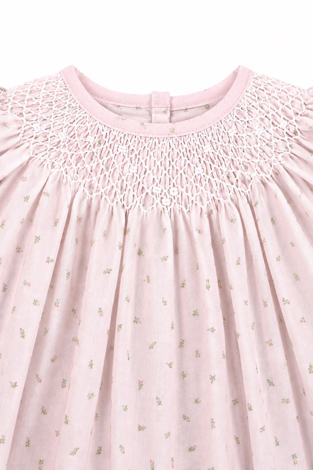 Carriage Boutique pink cotton baby dress featuring delicate rosebud print and intricate white hand-smocked detailing.