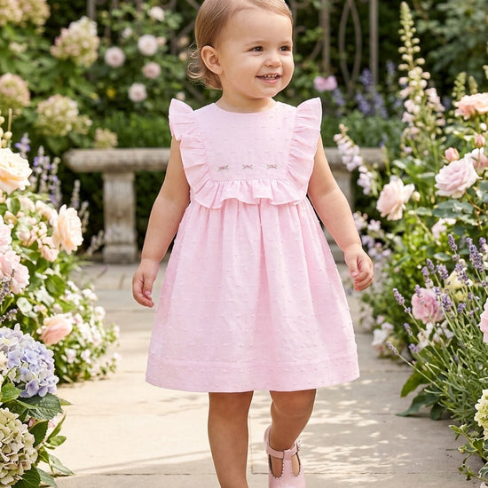 Carriage Boutique pink Swiss dot baby girl dress with ruffled sleeves and matching panty in a garden setting.