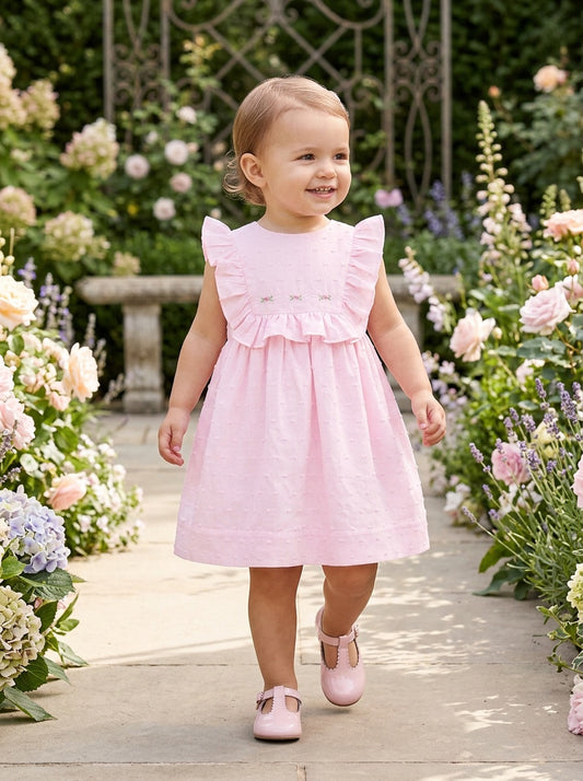 Carriage Boutique pink Swiss dot baby girl dress with ruffled sleeves and matching panty in a garden setting.