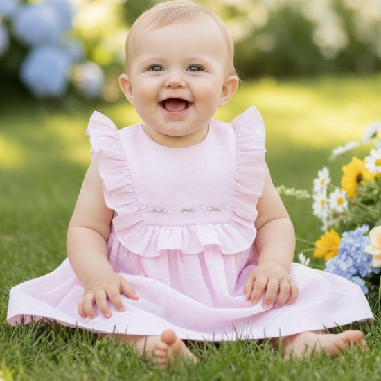 Carriage Boutique pink Swiss dot baby girl dress with ruffled sleeves and floral embroidery sitting on green grass