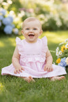 Carriage Boutique pink Swiss dot baby girl dress with ruffled sleeves and floral embroidery sitting on green grass