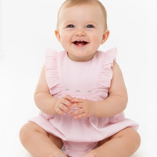 Carriage Boutique baby girl wearing a soft pink Swiss dot bubble romper with ruffled shoulders on a white background