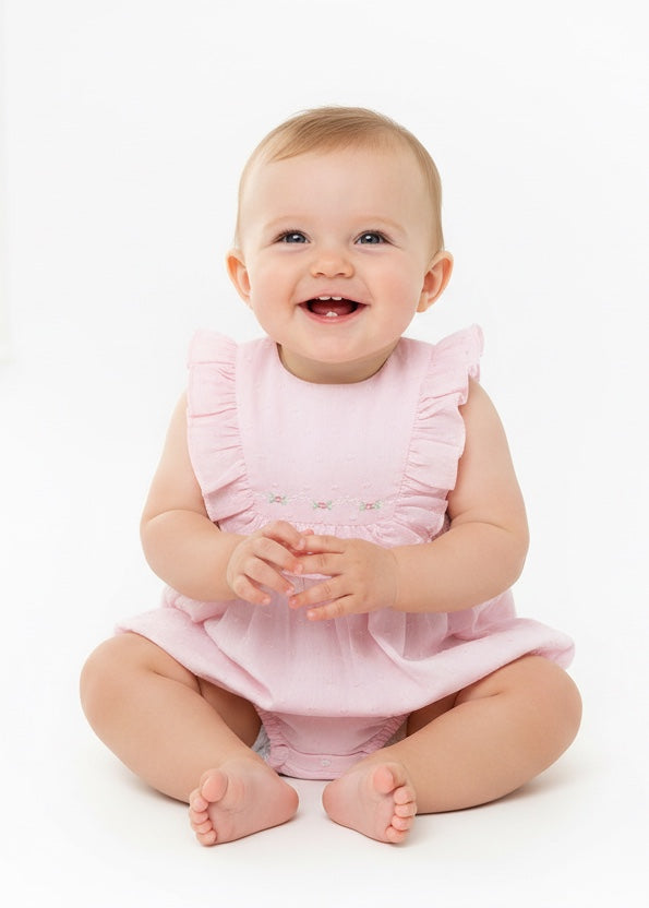 Carriage Boutique baby girl wearing a soft pink Swiss dot bubble romper with ruffled shoulders on a white background