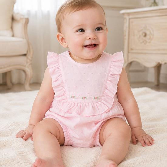 Carriage Boutique baby girl bubble romper in soft pink Swiss dot fabric with ruffled shoulders and floral embroidery.