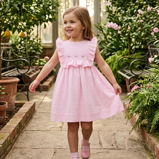 Carriage Boutique toddler girl wearing a pink Swiss dot dress with ruffled shoulders in a greenhouse setting