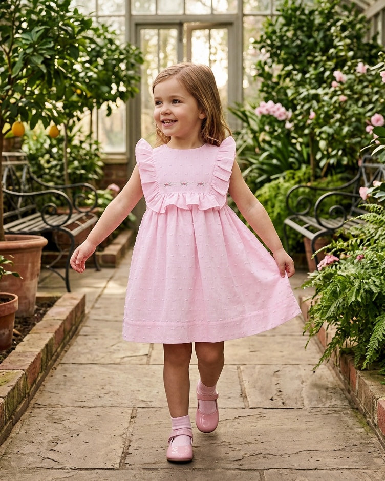Carriage Boutique toddler girl wearing a pink Swiss dot dress with ruffled shoulders in a greenhouse setting