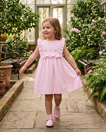 Carriage Boutique toddler girl wearing a pink Swiss dot dress with ruffled shoulders in a greenhouse setting