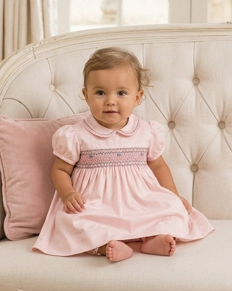 Carriage Boutique pink taffeta baby girl dress with hand-smocked floral waist and puffed sleeves on a tufted sofa