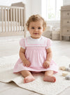 Carriage Boutique baby girl wearing a pink and white short sleeve dress with a classic sailor collar in a nursery.