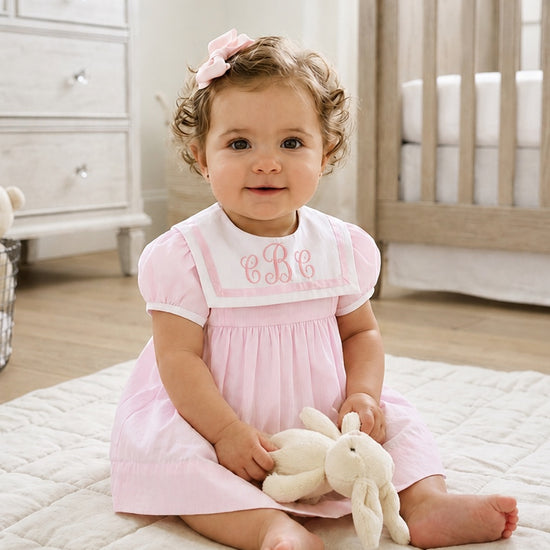 Carriage Boutique baby girl wearing a pink and white short sleeve dress with a monogrammed sailor collar and hair bow