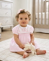 Carriage Boutique baby girl wearing a pink and white short sleeve dress with a monogrammed sailor collar and hair bow