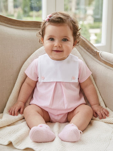 Carriage Boutique baby girl bubble romper in light pink and white cotton with a button bib, worn by a smiling baby.