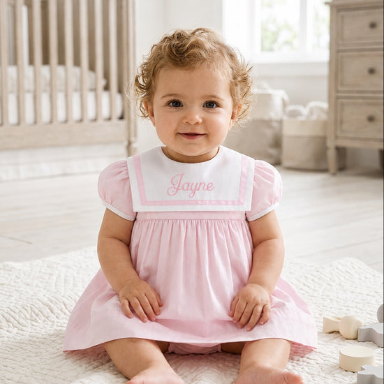 Carriage Boutique pink and white short sleeve toddler dress with embroidered sailor collar on a baby sitting on a rug