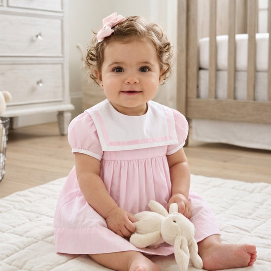 Carriage Boutique baby girl wearing a pink and white short sleeve dress with a sailor collar and matching hair bow
