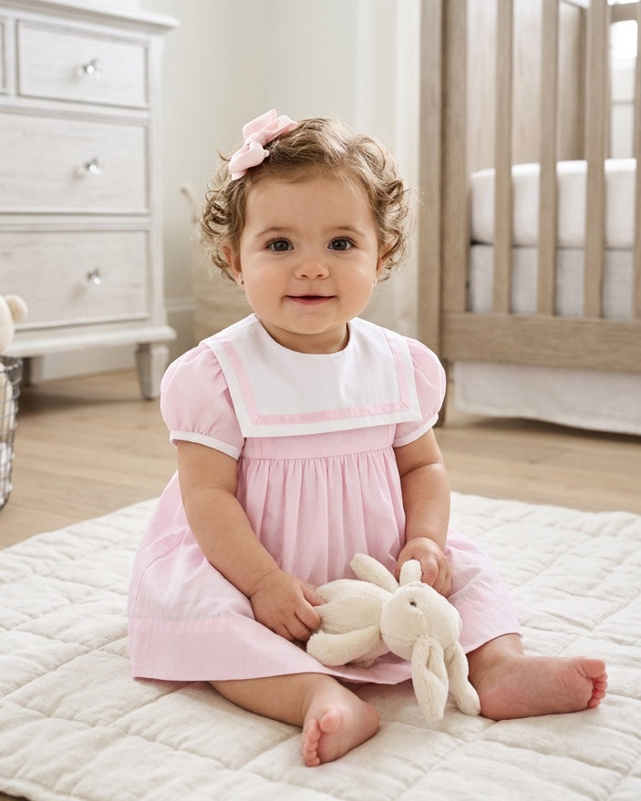 Carriage Boutique baby girl wearing a pink and white short sleeve dress with a sailor collar and matching hair bow