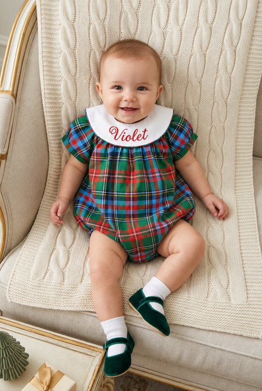 Carriage Boutique baby girl wearing a multicolor plaid bubble romper with a white monogrammed collar on a cream chair