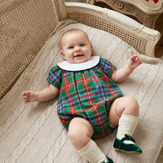 Carriage Boutique baby girl wearing a multicolor plaid bubble romper with a white collar, lying on a knit blanket.