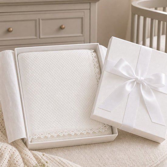 Carriage Boutique off-white quilted baby christening blanket with delicate lace trim inside a gift box.