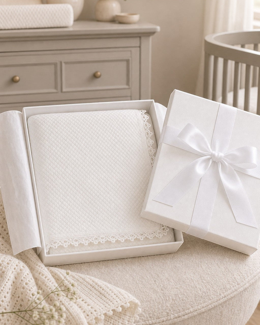 Carriage Boutique off-white quilted baby christening blanket with delicate lace trim inside a gift box.