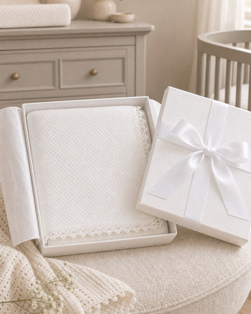 Carriage Boutique off-white quilted baby christening blanket with delicate lace trim inside a gift box.