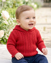 Carriage Boutique red cable knit hooded baby sweater worn by a smiling toddler in a garden setting