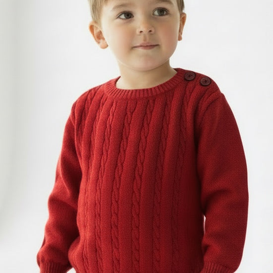 Toddler wearing a Carriage Boutique red cable knit crew neck sweater with shoulder buttons and beige trousers
