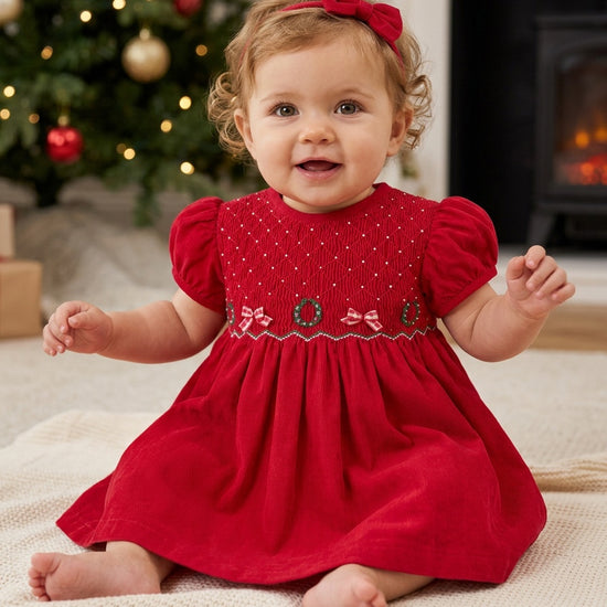 Carriage Boutique red corduroy baby girl dress with smocked bodice, Christmas wreath embroidery, and matching headband.
