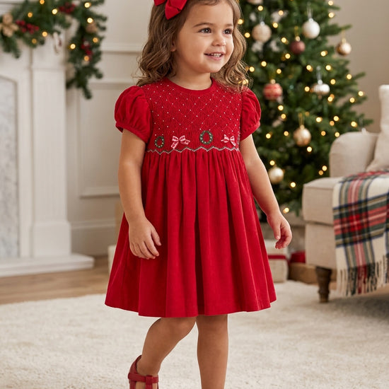 Carriage Boutique toddler girl wearing a red corduroy Christmas dress with smocked diamond and festive ribbon details.
