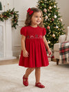 Carriage Boutique toddler girl wearing a red corduroy Christmas dress with smocked diamond and festive ribbon details.