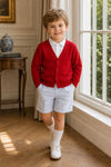 Carriage Boutique red cotton cashmere cardigan worn by a young boy with light blue shorts and white dress shoes