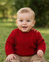 Carriage Boutique red fisherman knit pullover sweater worn by a smiling baby sitting on grass