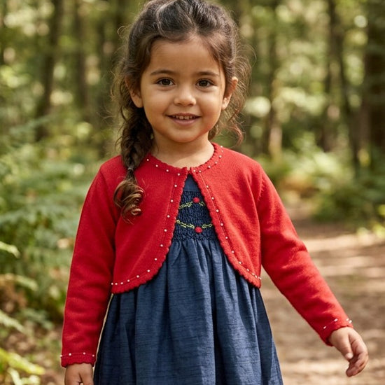Carriage Boutique red toddler bolero sweater with pearl trim worn over a blue dress in a forest setting.