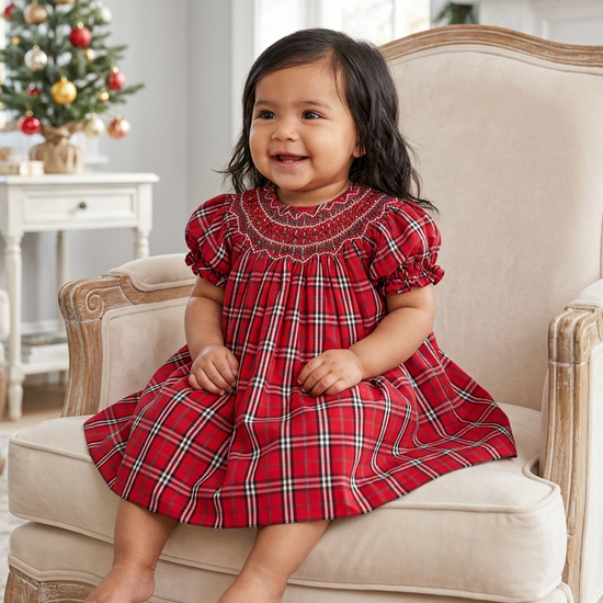 Carriage Boutique baby girl wearing a red and white plaid cotton bishop dress with hand smocking on the chest.