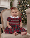 Carriage Boutique baby girl in a red plaid smocked dress with a white Peter Pan collar sitting on a vintage chair.