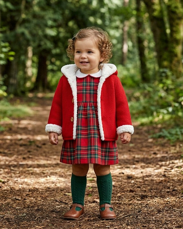 Toddler wearing a Carriage Boutique red knit hooded jacket with white sherpa lining over a plaid dress in a forest