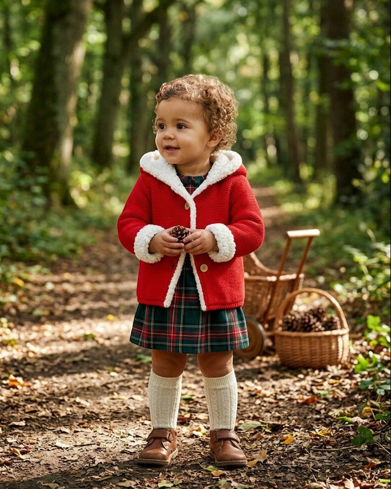 Toddler wearing a red Carriage Boutique sherpa-lined hooded knit jacket with a plaid dress in a forest setting