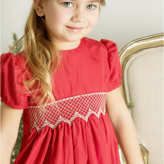 Young girl wearing a Carriage Boutique red taffeta dress with smocked diamond detailing and puffed sleeves