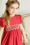 Young girl wearing a Carriage Boutique red taffeta dress with smocked diamond detailing and puffed sleeves