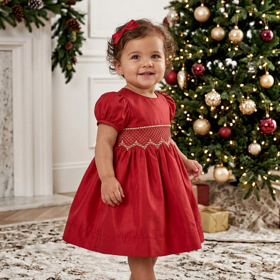 Carriage Boutique red taffeta baby dress with smocked diamond detailing and puffed sleeves near a Christmas tree